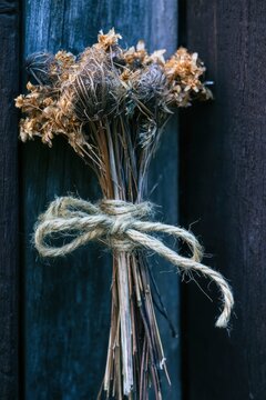 Dried wildflower stems tied with natural twine against a weathered dark wooden fence, showcasing delicate petals and rustic botanical elements in close-up composition