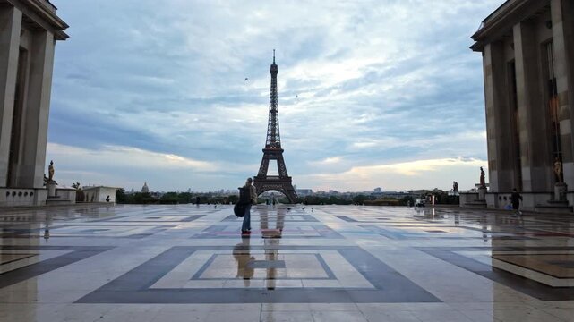 A single person walks across the wet patterned Trocad&eacute;ro esplanade as the Paris landmark rises under a soft blue morning sky.