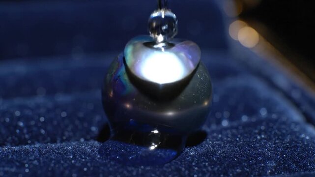 A shimmering black pearl with a sapphire blue water droplet resting in a luxurious dark blue velvet jewelry box