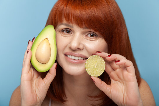 Radiant woman holding avocado and lime for vitamin facial and organic antioxidant skin detox isolated on blue background