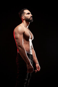 Muscular man posing showing fit athletic body with strong pectoral muscles and biceps under red rim light isolated over black background