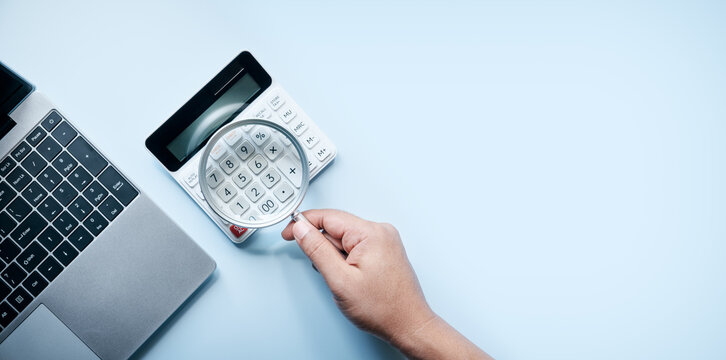 Financial analysis and business planning concept with calculator, magnifying glass, laptop, and hand on a blue desk, representing accounting, budgeting, auditing, investment research, and decisions