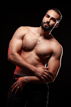 Sporty man posing with crossed arms showing shoulder definition and hairy chest with red rim lighting accentuating athletic body isolated over black background