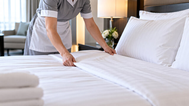 Hotel housekeeping worker making bed with fresh white linen in luxury guest room