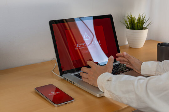 Man reacting to red security alert on laptop and smartphone