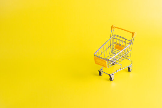 Yellow Miniature Shopping Cart with Copy Space on Yellow Background
