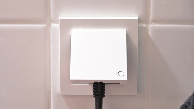 Close-up video of a person plugging an electrical power plug into a wall socket, representing electricity, power supply and everyday household use.