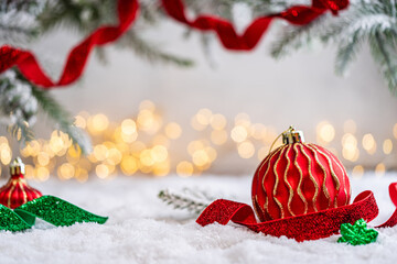Naklejka premium A Christmas background featuring a red bauble with a golden wave pattern beside a sparkling red ribbon beneath frosted pine on snow, softly lit by warm twinkling lights with copy space.