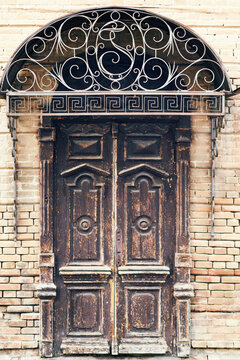Ornate antique wooden door with wrought iron decoration set in brick wall