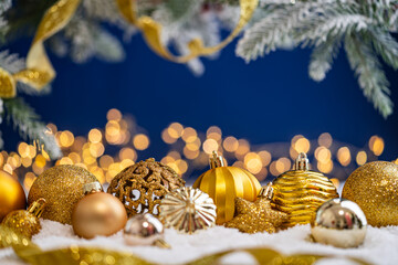 Naklejka premium A Christmas background featuring an abundant array of gold baubles, an ornate filigree ornament, and a star wrapped in ribbon on snow, set against deep blue with twinkling lights and copy space.