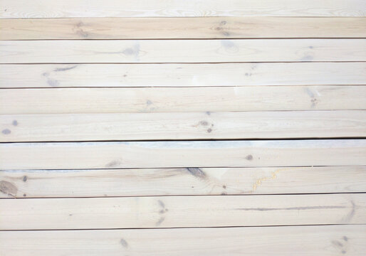 A wooden background made of white or beige planks. Natural wood texture, knots, and grain lines. Even, dark gaps between the planks, with wood particles or sawdust on the right side.