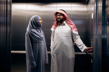 Muslim couple wearing traditional clothing, a woman in hijab and a man in thawb and keffiyeh, using an elevator © Petro