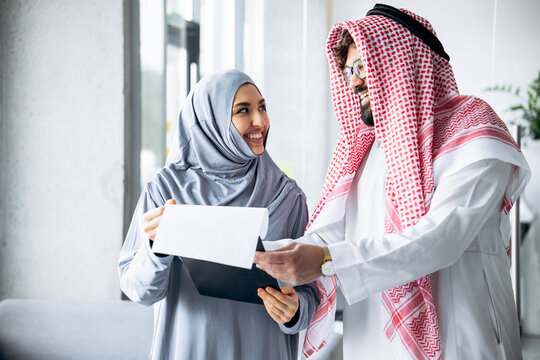 Muslim businesswoman and businessman smiling, collaborating, and reviewing documents in a modern office environment