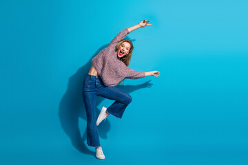Fototapeta premium Young chic woman jumps in casual sweater jeans against blue background joy energy fashion lifestyle beauty advertising shopping campaigns