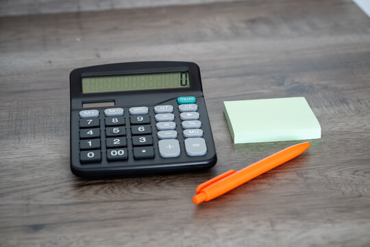 Calculator with leather wallet sticky note pad and orange pen on wooden desk