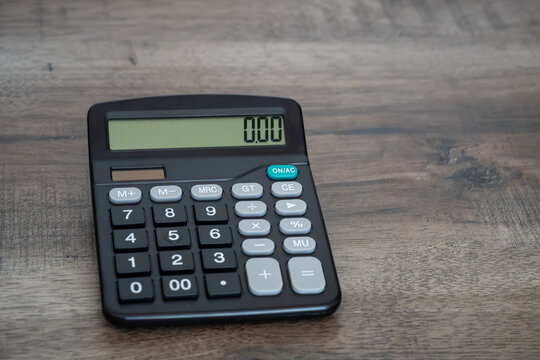 Black electronic calculator displaying zero on wooden office desk