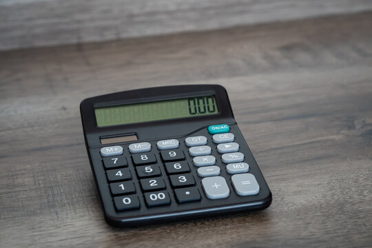 Black electronic calculator displaying zero on wooden office desk