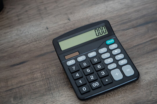 Black electronic calculator displaying zero on wooden office desk