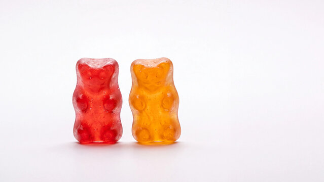 Gummy bears in red and orange colors stand side by side on a plain white background with soft shadow.