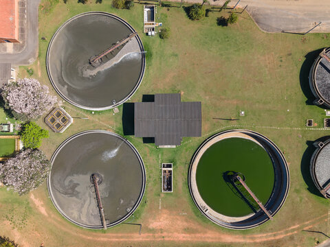 Aerial view of a water treatment plant with circular sedimentation tanks and industrial buildings surrounded by rural landscape