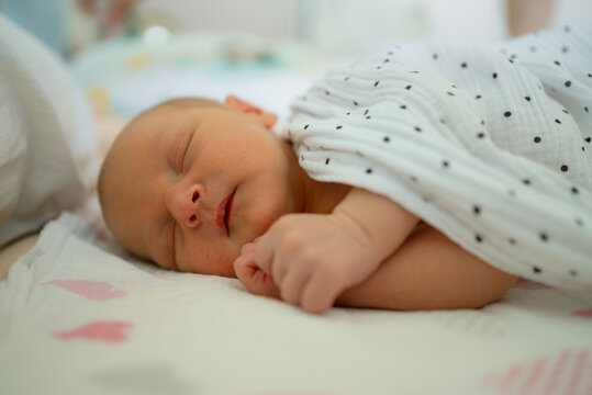 Newborn baby boy sleeping peacefully, wrapped in a soft swaddling cloth with black polka dots, resting on a blanket with faint heart patterns, symbolizing innocence and early childhood