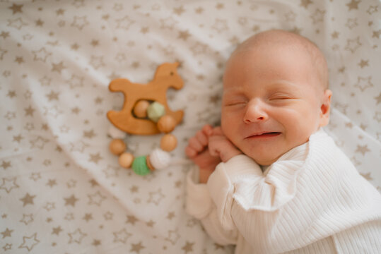 Newborn baby happily sleeping on star patterned bedding with a wooden rocking horse rattle, dreaming peacefully and showing a soft smile in slumber, capturing moments of infancy and growth