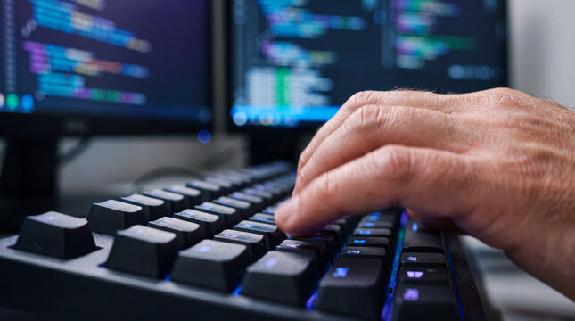 Professional software developer typing on mechanical keyboard with focused concentration in dark workspace with glowing screen code