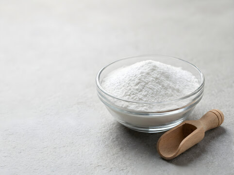 Pure creatina powder in a small glass bowl with a wooden scoop on a gray stone background