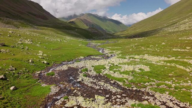 Aerial tracking shot of mountain stream flowing through a green valley