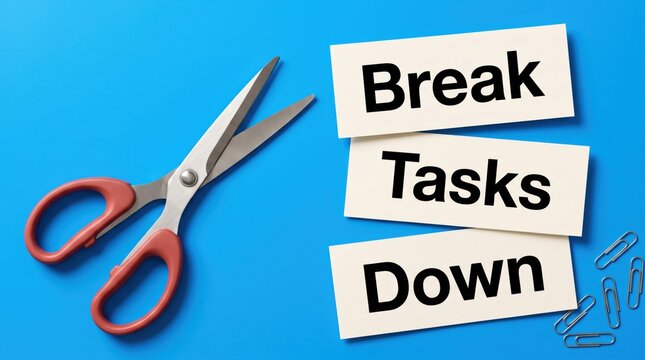 Scissors beside paper cards with text break tasks down placed on a vibrant blue background representing productivity and efficient planning