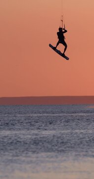 Kite surfer riding and jumping on sea water with warm sunset light