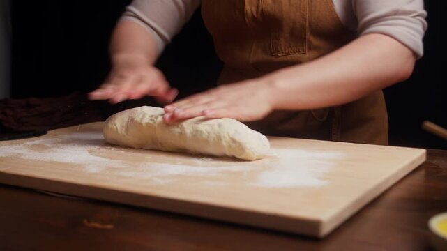 Woman kneading homemade dough on a floured wooden board.Close up of a woman kneading fresh dough by hand on a floured wooden board, showing traditional homemade baking and food preparation in a warm