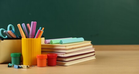 Different stationery on wooden table near chalkboard, closeup. Space for text © New Africa