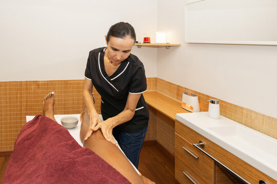 Woman therapist giving leg massage to client in spa