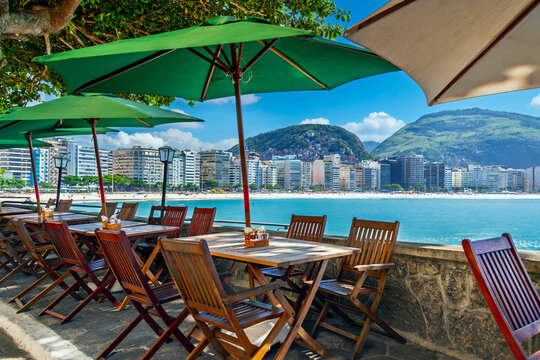 Outdoor cafe seating at Copacabana Fort, overlooking the beach, city skyline, and mountains on a sunny day in Rio de Janeiro, Brazil.