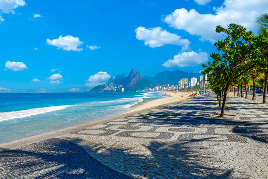 Beautiful Ipanema beach in Rio de Janeiro featuring the iconic mosaic boardwalk, blue ocean, and Two Brothers mountains on a bright day.