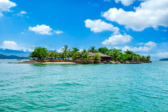 Ilha Rasa in Paraty Bay, Rio de Janeiro. A tropical island featuring rustic seaside buildings, palm trees, and green waters under a bright blue sky.