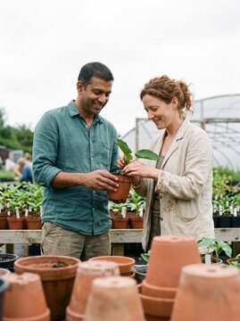 Diverse male and female gardeners smiling while examining a potted plant in an outdoor nursery