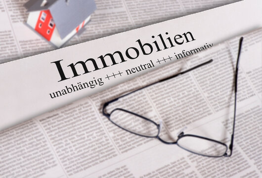 Auf einer Tageszeitung mit &Uuml;berschrift Immobilien liegt eine Brille mit einem Modellhaus