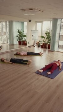 Yoga class doing corpse pose in a bright studio.