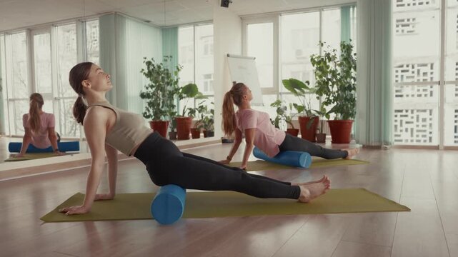 Two women use foam rollers for leg muscle release in a fitness class