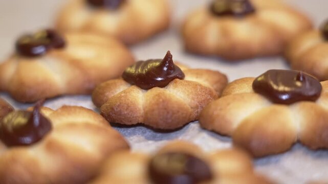 Close-up view of freshly baked cookies with chocolate topping, arranged on parchment paper. The cookies have a golden-brown color and a decorative shape, showcasing their delicious appearance