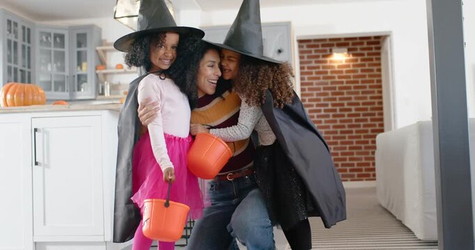 Costumed African American mother with girls fixing witch hats in kitchen then guiding with pumpkins