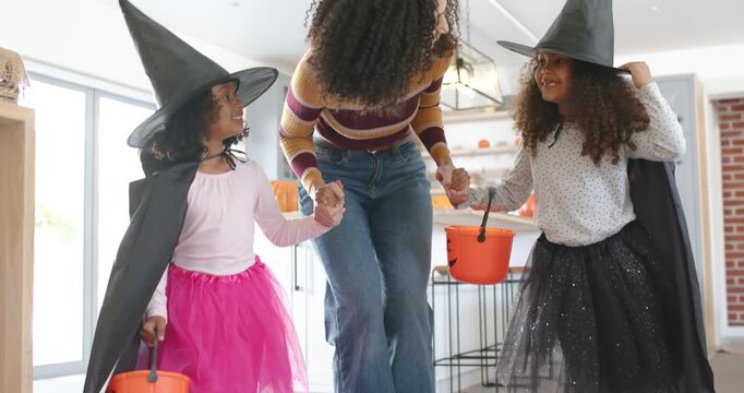Low camera pulling back African American mom stepping holding hands pumpkin pails kitchen for candy