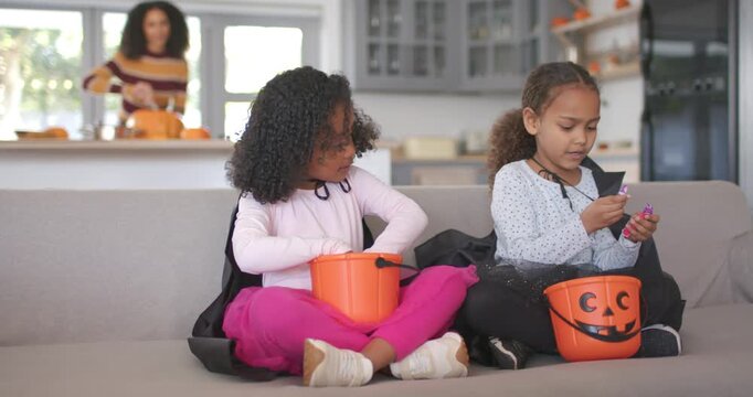 African American family girls sorting candy from pumpkin pails on couch while mom carving pumpkin