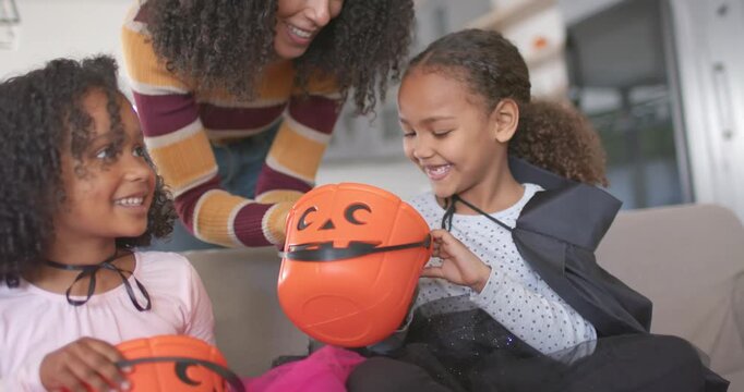 African American mom and daughters sitting on sofa kids tipping treat buckets mom handing candy