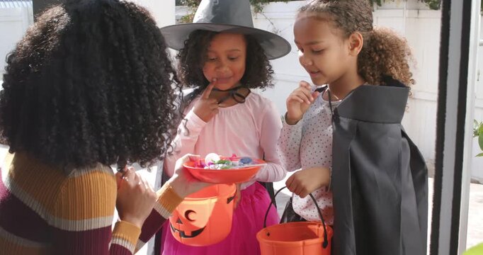 African American girls reaching into red candy bowl on porch after woman opening door for candy