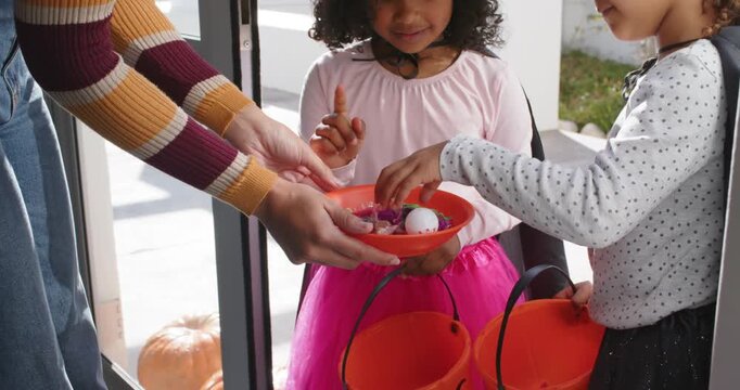 African American girls witch-hat taking candy from bowl on porch adult opening door at Halloween
