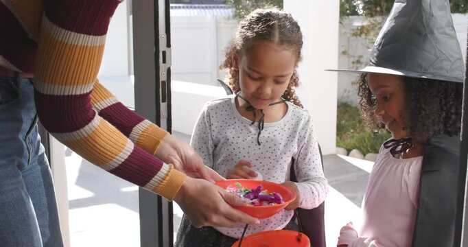 African American children wearing capes reaching into orange bowl at door as host offering treats