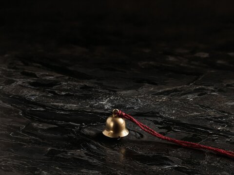 Antique brass bell on dark textured surface with red string  